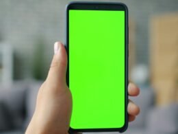 Hand hält ein Smartphone mit grünem Bildschirm, geeignet als Symbolbild für mobile Technologien und digitale Anwendungen.