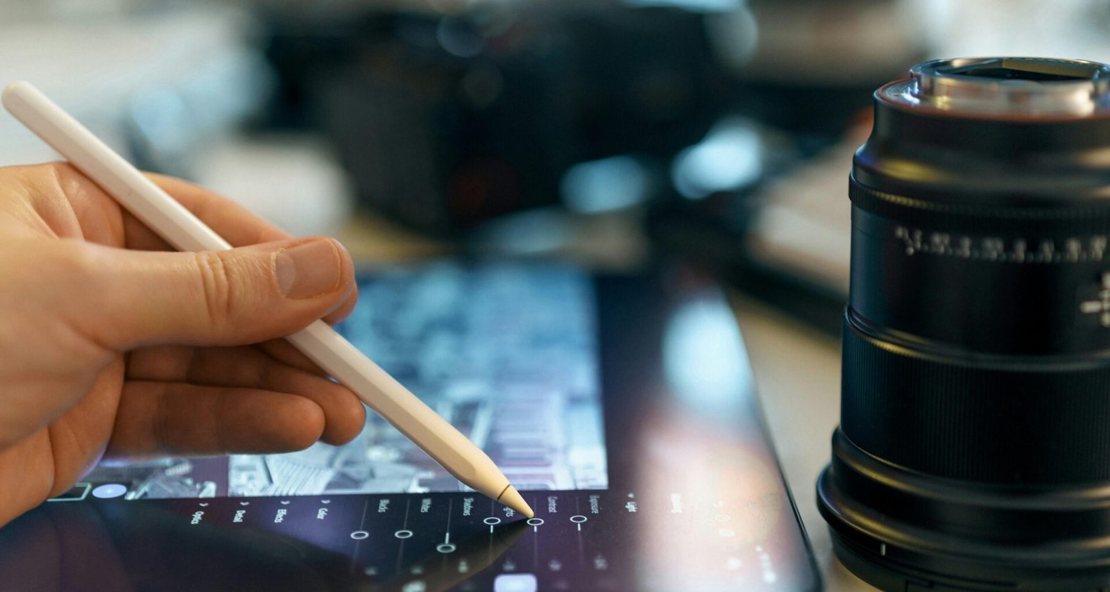 Hand mit Stylus bedient Tablet neben Kameraobjektiv – digitale Arbeit und Technik im Online-Marketing