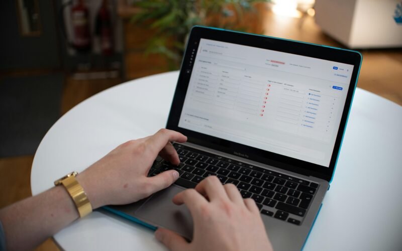 Hände tippen auf einem Laptop, auf dessen Bildschirm eine Tabellenkalkulation geöffnet ist