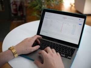 Hände tippen auf einem Laptop, auf dessen Bildschirm eine geöffnete Tabellenkalkulation zu sehen ist.