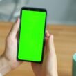 Zwei Hände halten ein Smartphone mit grünem Bildschirm – perfekt für Themen rund um digitale Technologien und Online-Marketing.