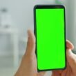 Zwei Hände halten ein Smartphone mit grünem Bildschirm, geeignet für Themen über mobile Technologien oder App-Entwicklung