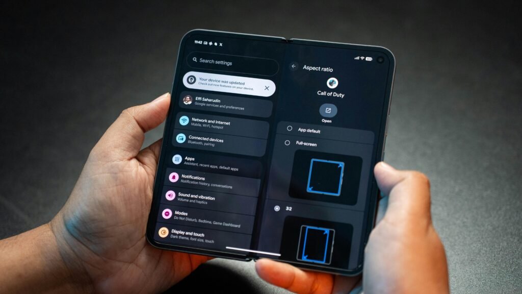 Zwei Hände halten ein aufklappbares Smartphone, das auf dem Bildschirm das Menü Einstellungen anzeigt.