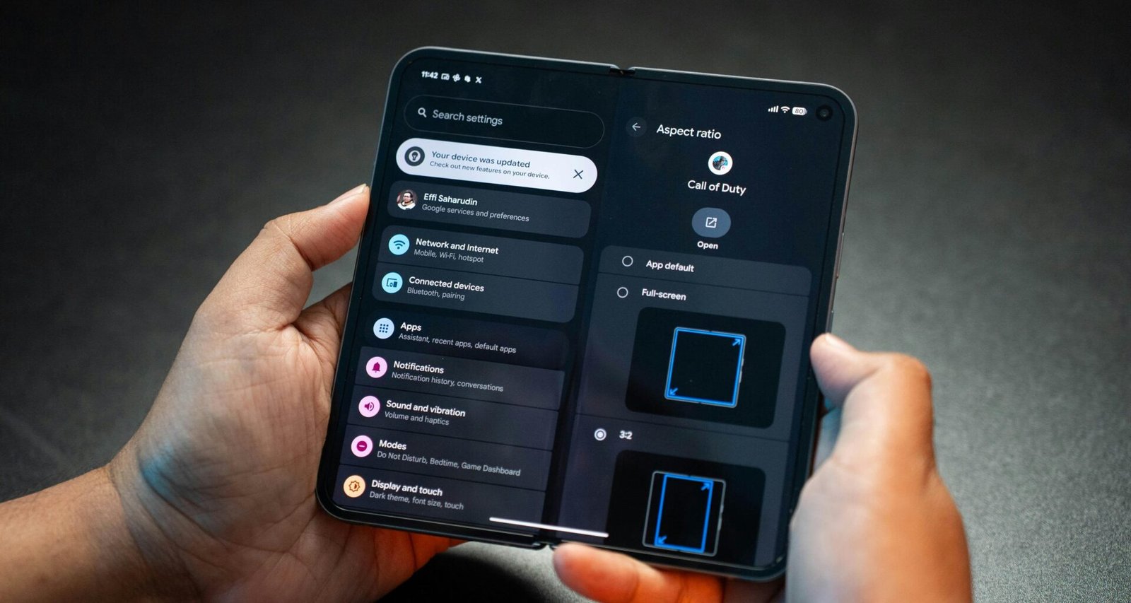 Zwei Hände halten ein aufklappbares Smartphone, das auf dem Bildschirm das Menü Einstellungen anzeigt.