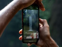 Zwei Hände halten ein Smartphone, das einen Wasserfall filmt; moderner Technologieeinsatz in der Natur