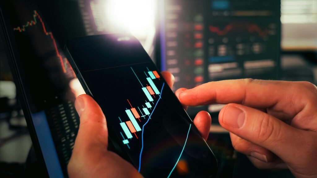 Zwei Hände halten ein Smartphone, auf dessen Bildschirm aktuelle Börsendaten und Finanzdiagramme angezeigt werden.