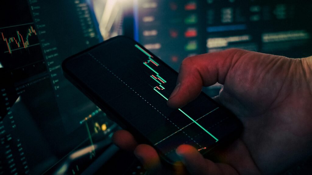 Trader betrachtet Börsenkurse und Marktanalysen auf einem Smartphone, während parallel Daten auf dem Telefon verfolgt werden