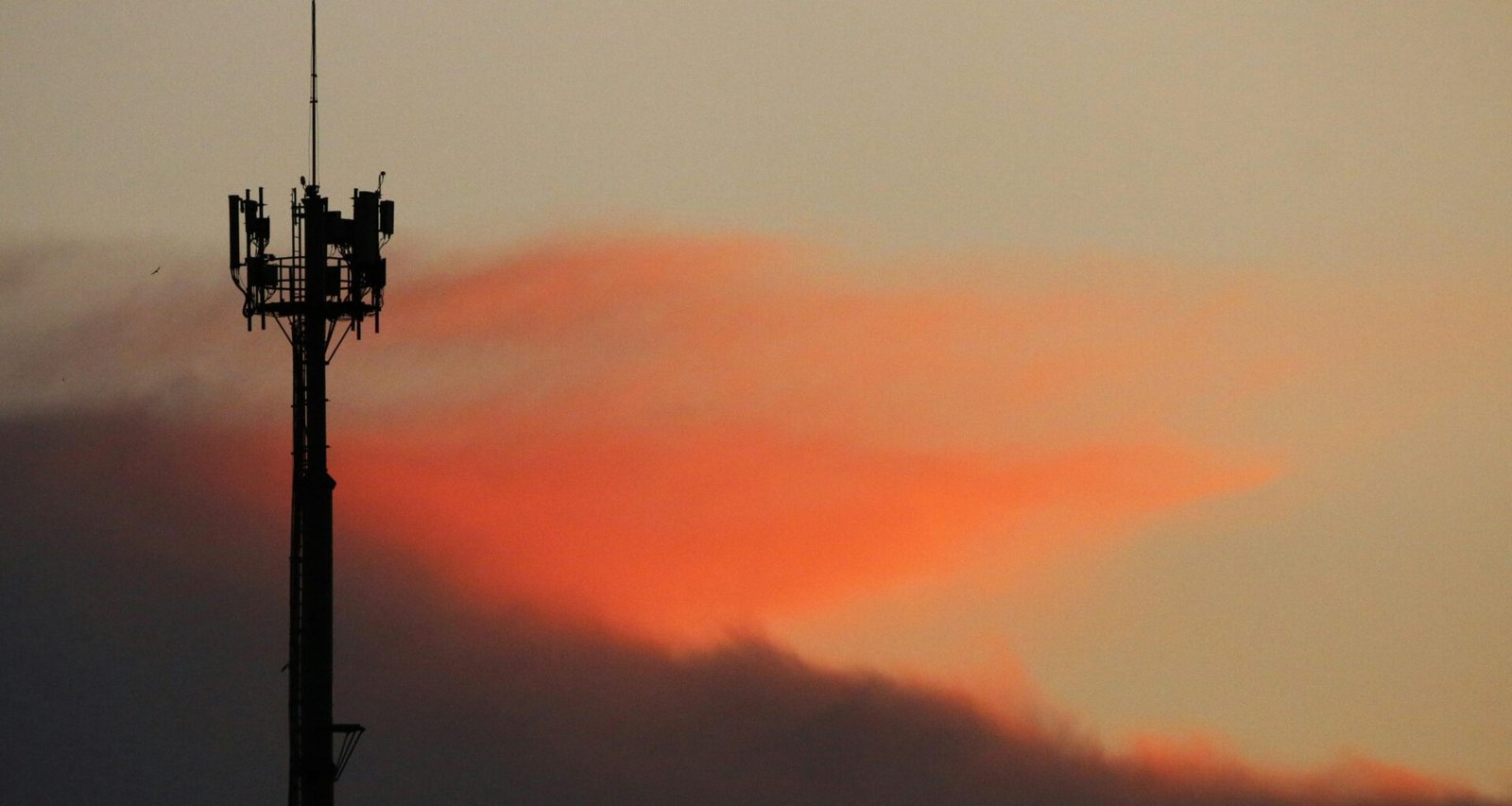 Ein Mobilfunkmast als Silhouette vor einem farbigen Sonnenuntergangshimmel, Fokus auf moderne Kommunikationsinfrastruktur.