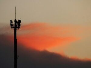 Ein Mobilfunkmast als Silhouette vor einem farbigen Sonnenuntergangshimmel, Fokus auf moderne Kommunikationsinfrastruktur.