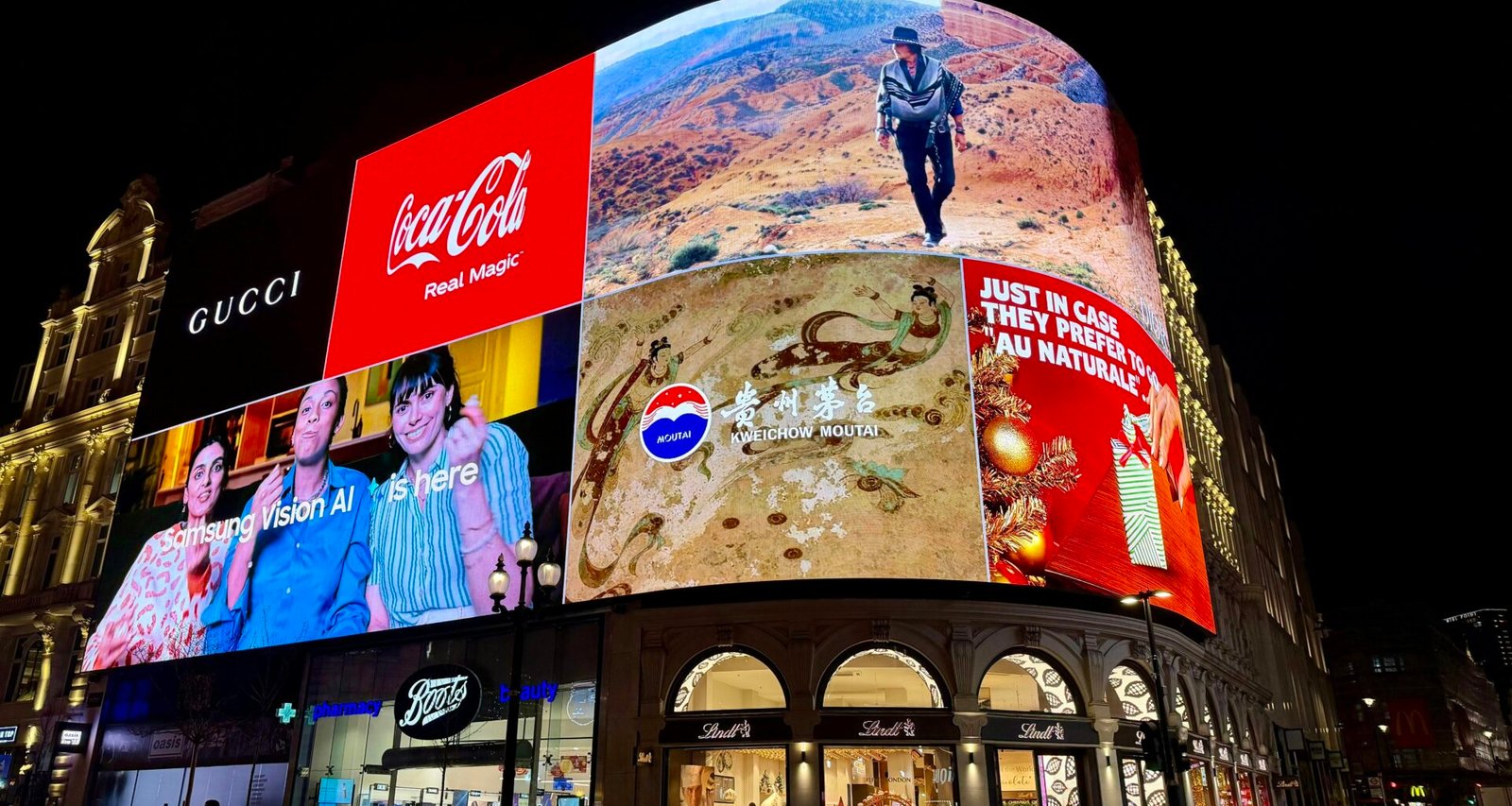 Mehrere digitale Werbetafeln leuchten nachts auf der Fassade eines städtischen Gebäudes und ziehen vorbeigehende Blicke an.