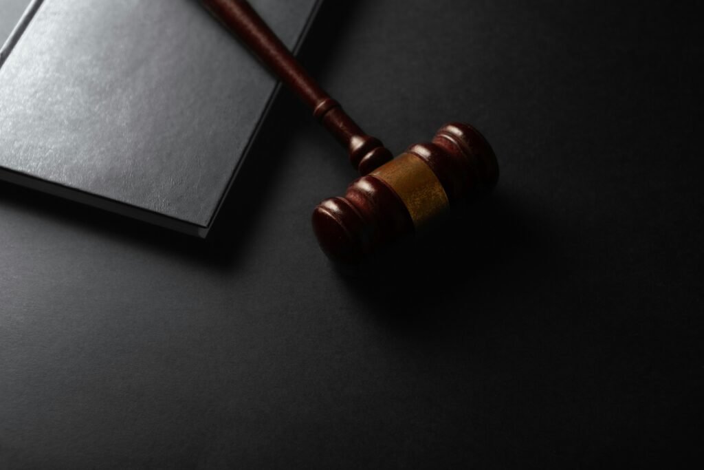 Ein hölzerner Richterhammer ruht neben einem aufgeschlagenen Buch auf dunklem Untergrund, Fokus auf Recht und Gesetz