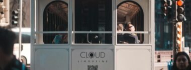 Mehrere Personen fahren tagsüber mit einer Straßenbahn durch das urbane Zentrum einer Großstadt.