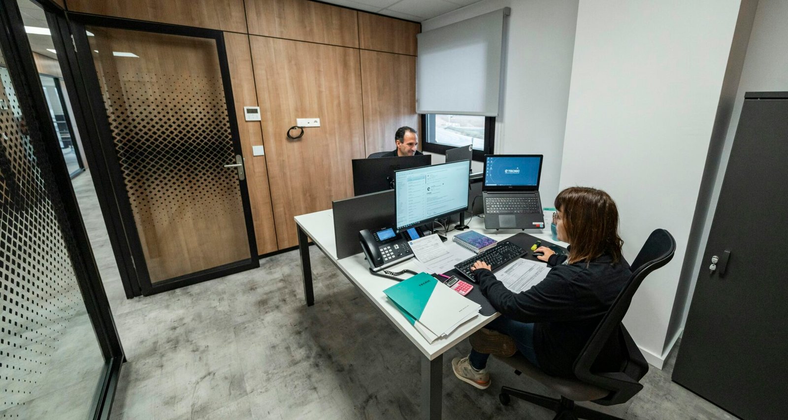 Menschen arbeiten gemeinsam an Schreibtischen in einem modernen Büro mit offenem Raumkonzept und technischer Ausstattung.