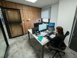 Menschen arbeiten gemeinsam an Schreibtischen in einem modernen Büro mit offenem Raumkonzept und technischer Ausstattung.