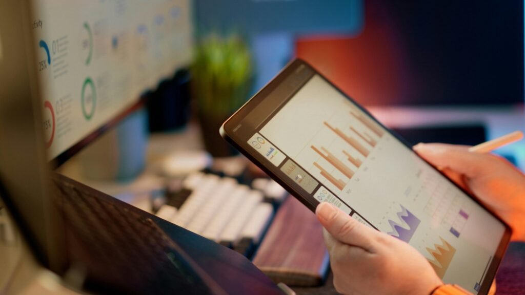 Person wertet auf einem Tablet Finanzdaten aus, grafische Auswertungen und Tabellen in moderner Arbeitsumgebung sichtbar