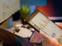 Person analysiert Finanzdaten auf einem Tablet, digitale Diagramme und Zahlen sichtbar, Fokus auf Datenauswertung