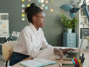 Junge Frau sitzt an einem Schreibtisch in einem hellen Büro und arbeitet konzentriert am Computer