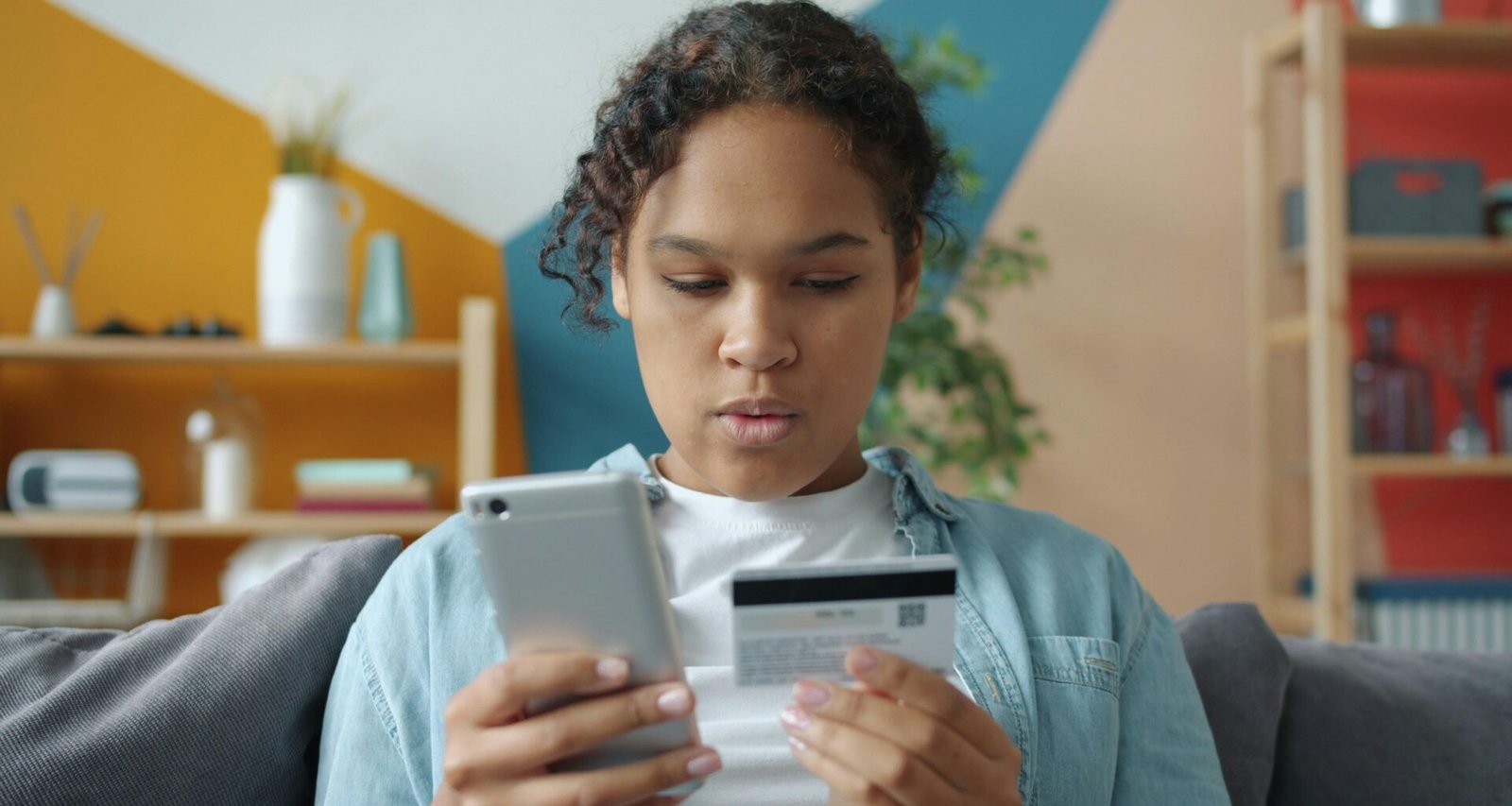 Junge Frau hält eine Kreditkarte und ein Smartphone in einem modernen Innenraum, bereit für Online-Zahlungen.