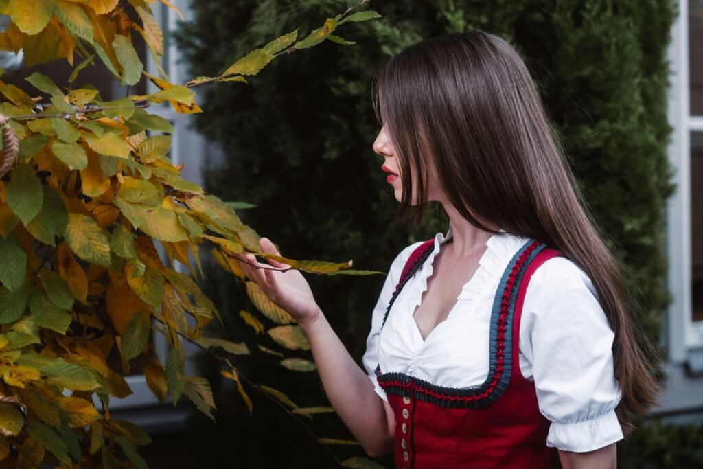 Junge Frau in traditioneller Kleidung berührt herbstliche Blätter an einem Baum vor natürlichem Hintergrund