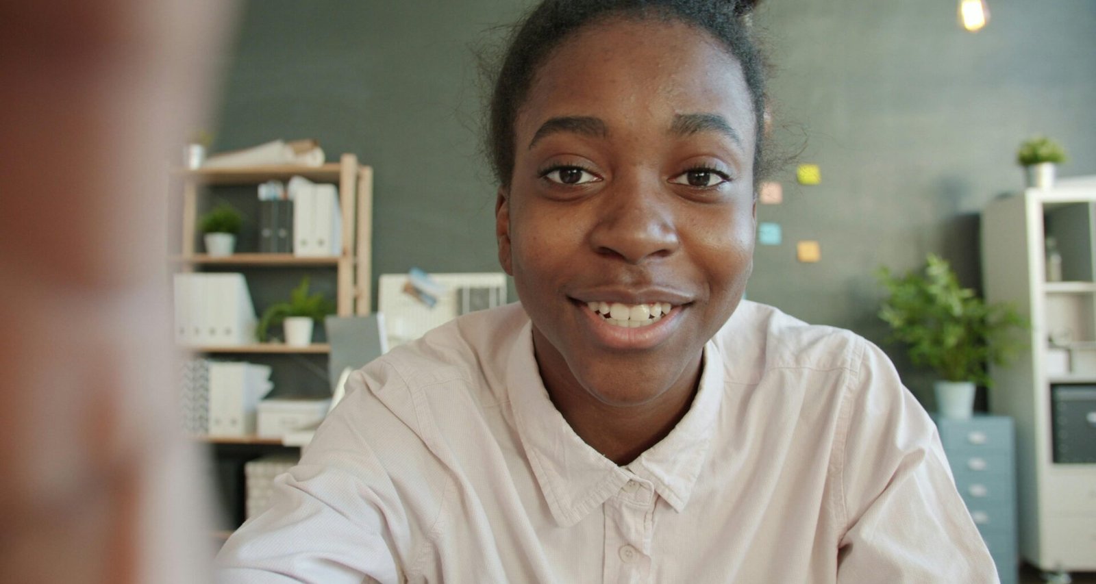 Junge Frau sitzt lächelnd an einem Schreibtisch im hellen Büro mit Laptop und Notizbuch vor sich