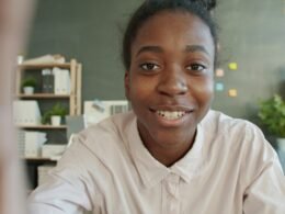 Junge Frau sitzt lächelnd an einem Schreibtisch im hellen Büro mit Laptop und Notizbuch vor sich