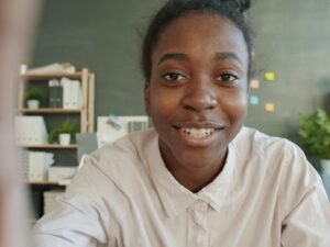 Junge Frau sitzt lächelnd an einem Schreibtisch im hellen Büro mit Laptop und Notizbuch vor sich