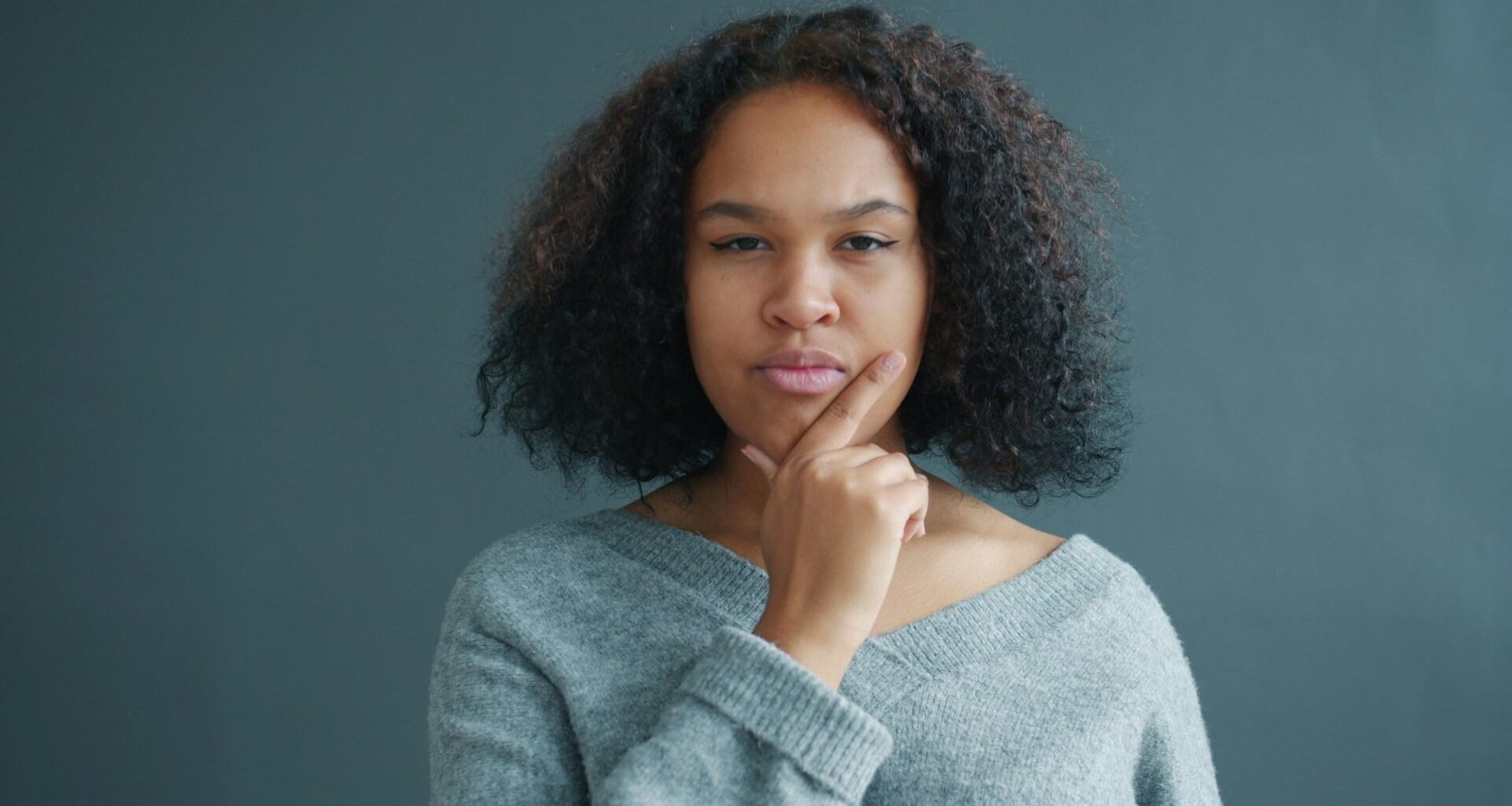Junge Frau mit Hand am Kinn, nachdenklicher Gesichtsausdruck, nach links blickend, aufgenommen vor neutralem Hintergrund