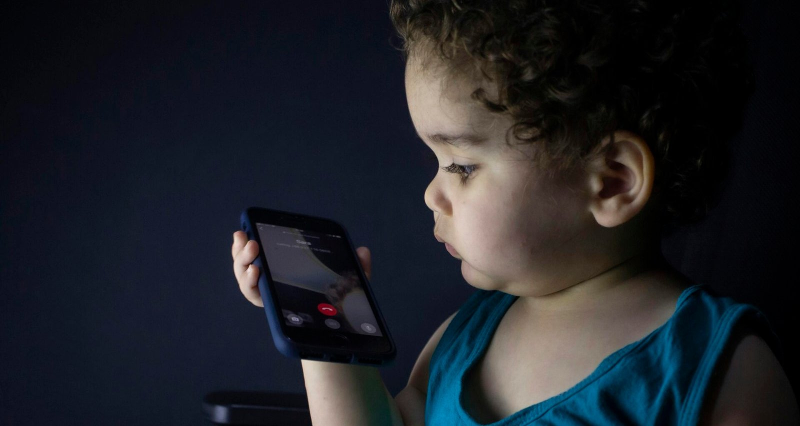 Junge im blauen Tanktop hält ein schwarzes Smartphone in den Händen und schaut auf das Display, neutraler Hintergrund