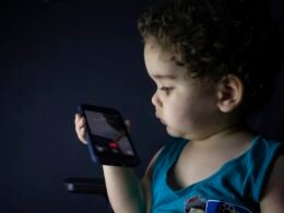 Junge im blauen Tanktop hält ein schwarzes Smartphone in den Händen und schaut auf das Display, neutraler Hintergrund