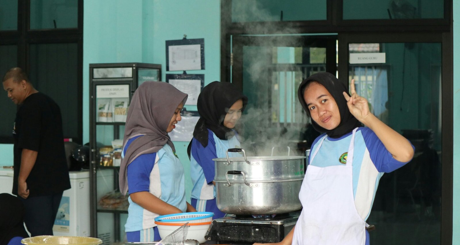 Gruppe junger Menschen kocht und dämpft Lebensmittel in moderner Küche. Küchenutensilien und Zutaten sind auf dem Tisch verteilt.