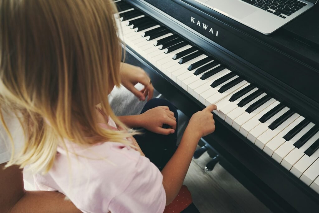 Junges Mädchen spielt auf einem Klavier, während ein geöffneter Laptop direkt daneben steht