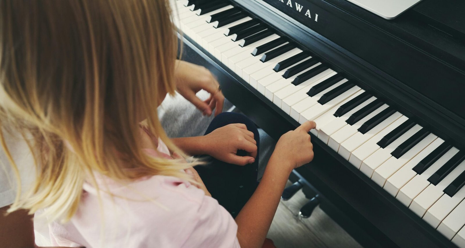 Junges Mädchen spielt auf einem Klavier, während ein geöffneter Laptop direkt daneben steht