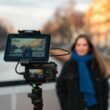 Kamera-Setup auf einem Stativ mit Frau im Hintergrund nahe einem Kanal, Fokus auf Technik und kreative Arbeit