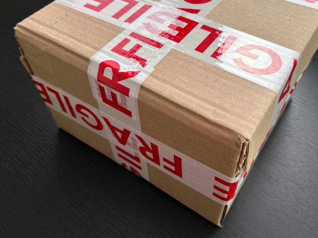 Ein brauner Karton, der mit rotem Fragile-Klebeband versiegelt wurde, steht als Symbol für sicheren Versand empfindlicher Produkte.