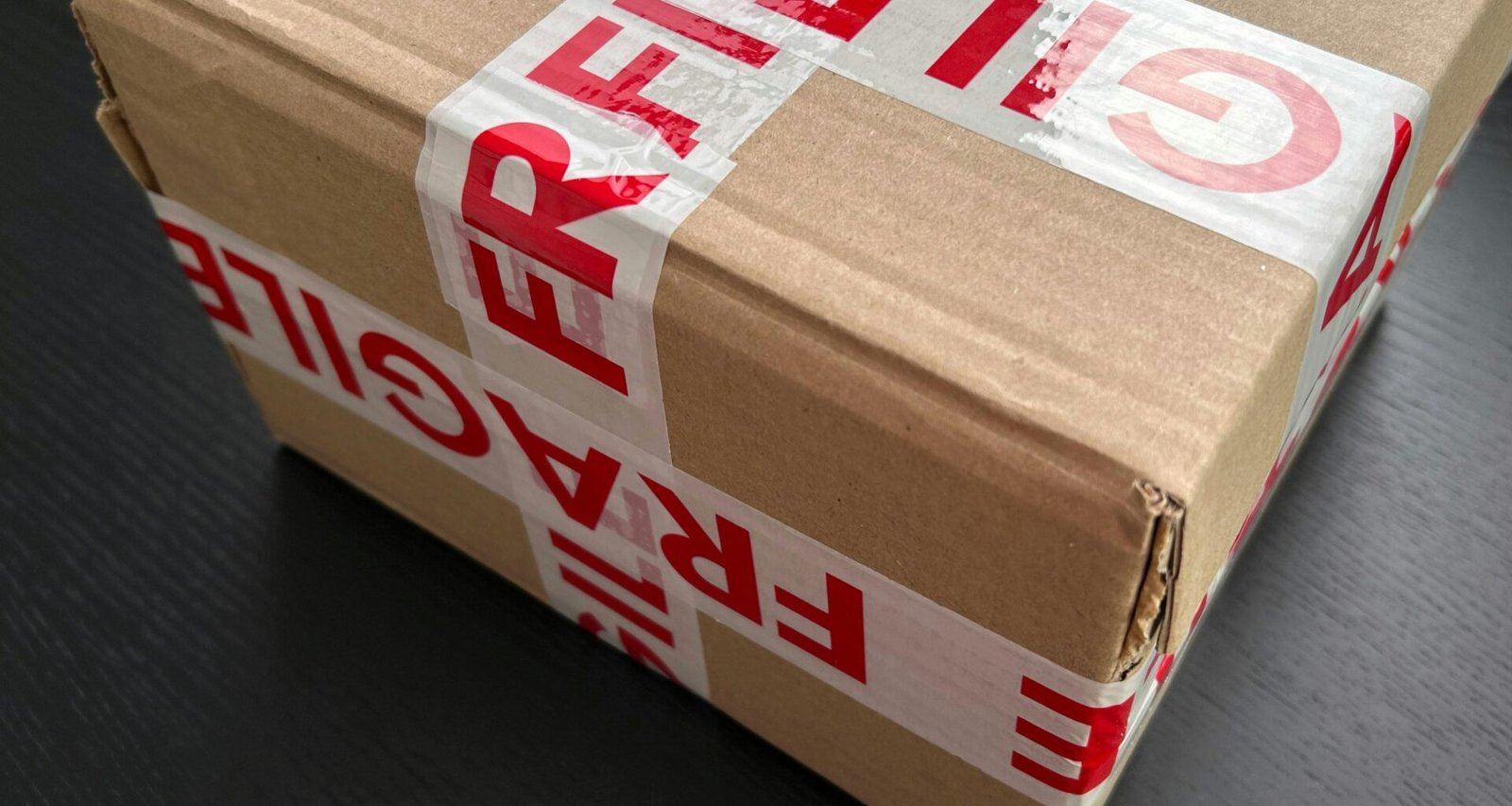 Ein brauner Karton, der mit rotem Fragile-Klebeband versiegelt wurde, steht als Symbol für sicheren Versand empfindlicher Produkte.