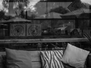 Mehrere Kissen liegen auf einer Holzbank. Im Fenster daneben spiegeln sich Konturen der Umgebung wider.