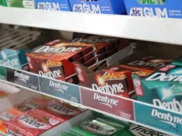 Ein KitKat Schokoriegel liegt auf einem weißen Regal. Klare Präsentation des Produkts, Fokus auf Verpackung und Form.