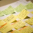 Mehrere bunte Sticky Notes mit handgeschriebenem Text liegen nebeneinander auf einer ebenen Fläche arrangiert.