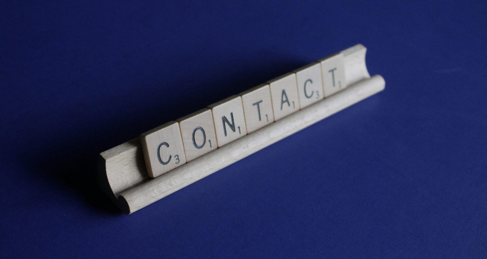 Scrabble-Spielsteine, die das Wort Kontakt buchstabieren, auf einem Tisch arrangiert; Fokus auf Buchstabensteine