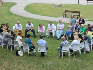Menschen sitzen im Kreis auf Stühlen auf einer grünen Wiese, geeignet als Symbol für Zusammenarbeit oder Workshop im Freien