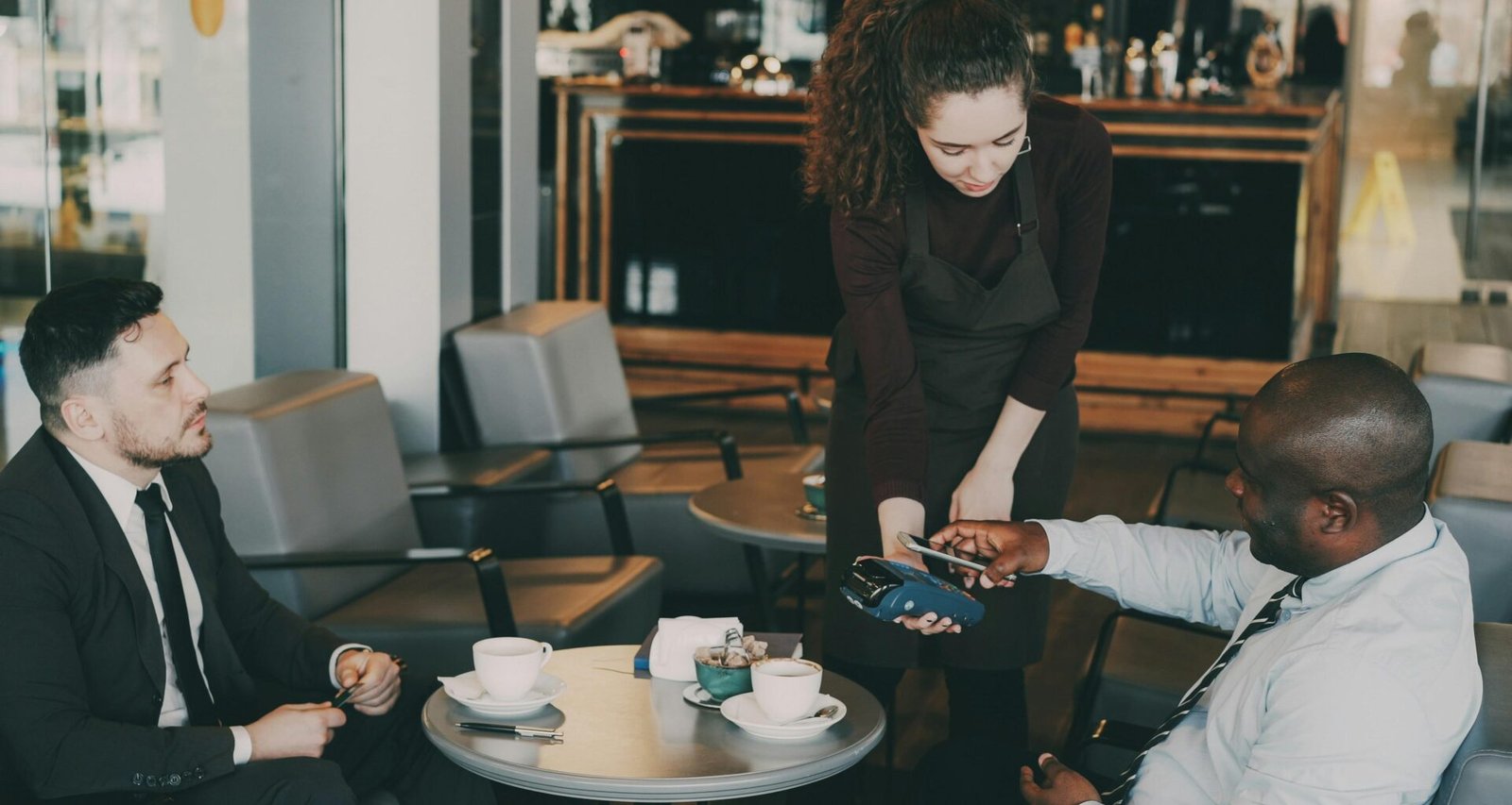 Kunde zahlt mit Kreditkarte an der Theke eines Cafés, Fokus auf das Kartenterminal und den Bezahlvorgang.