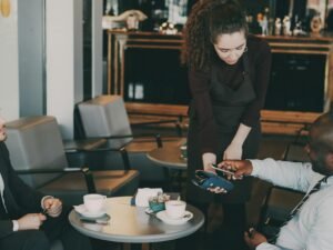 Kunde zahlt mit Kreditkarte an der Theke eines Cafés, Fokus auf das Kartenterminal und den Bezahlvorgang.