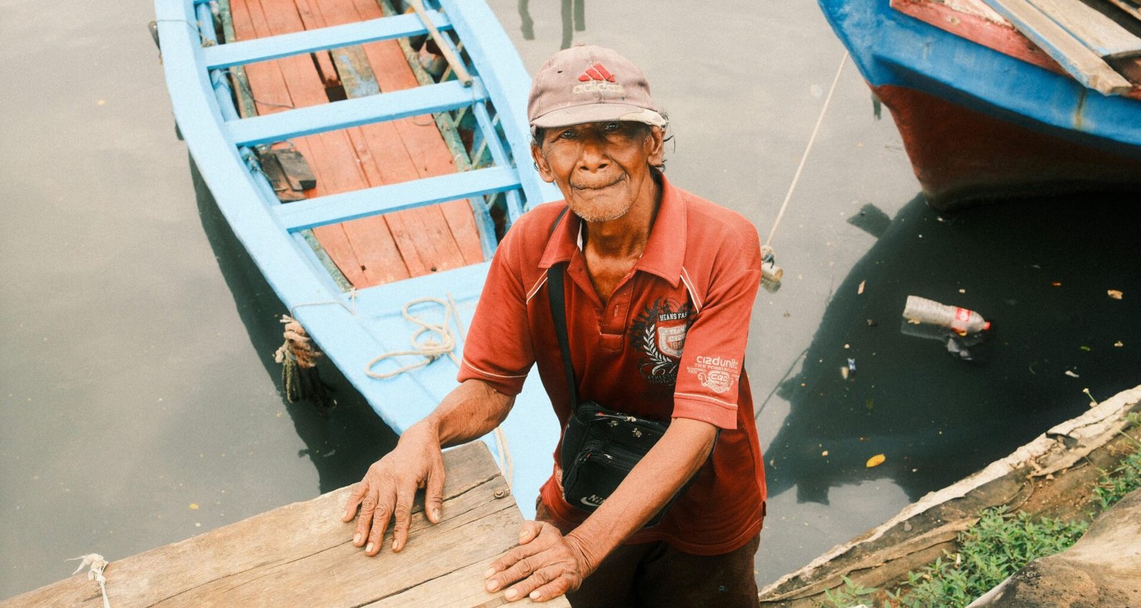 Ein lächelnder Mann steht nahe an Booten am Hafen, Wasser im Hintergrund, aufgenommen bei Tageslicht