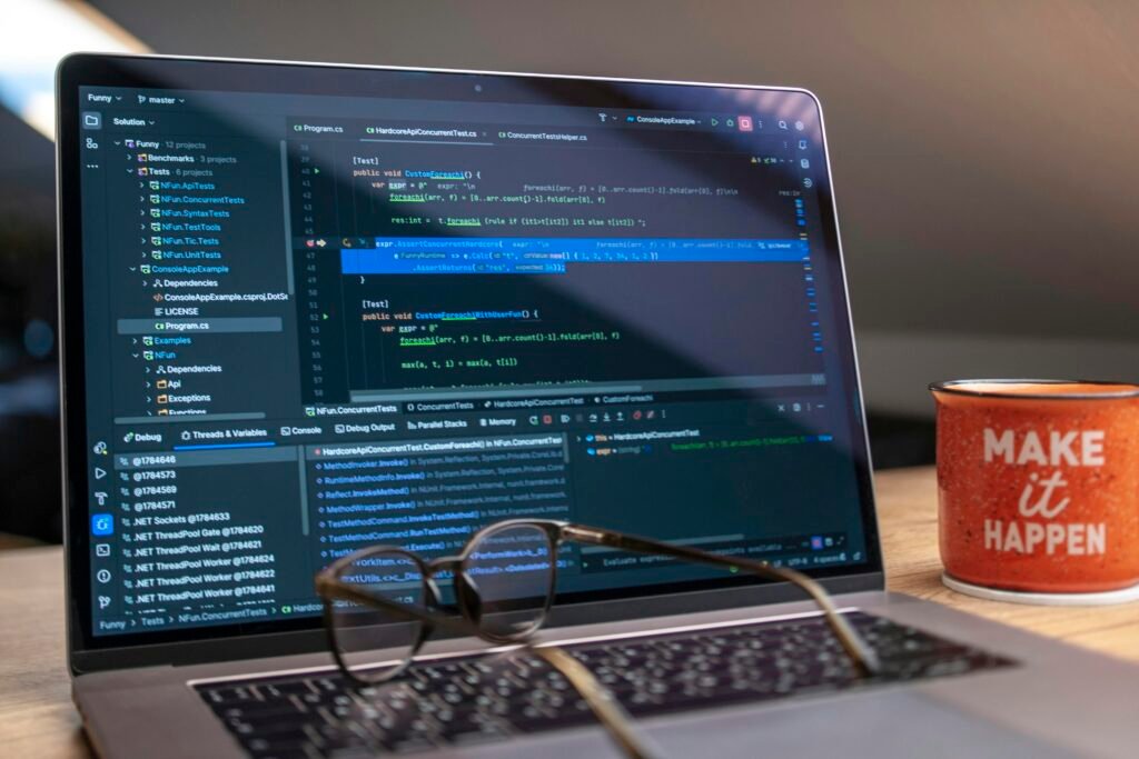 Laptop mit offenem Code auf dem Bildschirm, daneben eine Brille und eine Kaffeetasse auf einem Schreibtisch