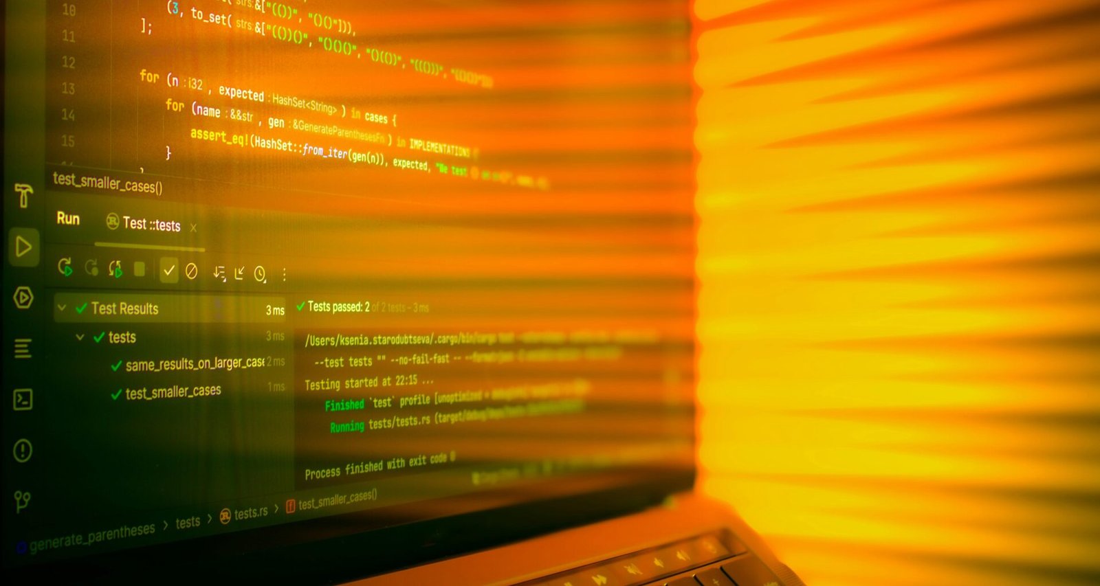 Laptop-Bildschirm mit geöffnetem Code-Editor und orangefarbenem Leuchten im Hintergrund, geeignet für IT-Themen