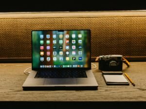 Laptop, Kamera und Notizblock auf hölzernem Schreibtisch für digitales Arbeiten und kreative Planung in moderner Umgebung