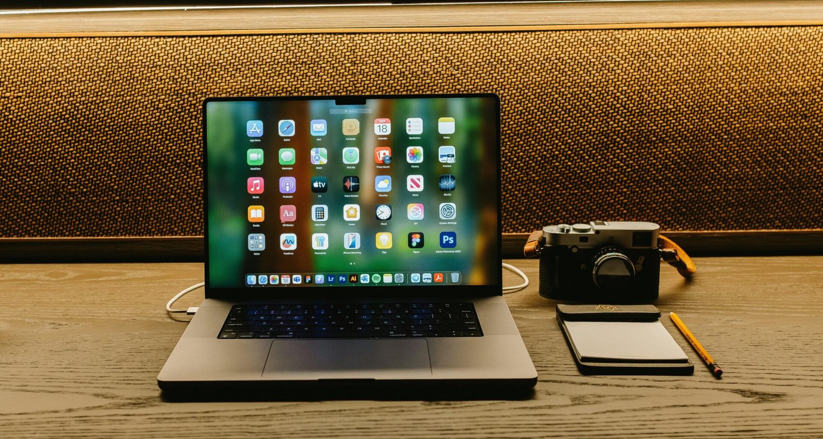 Laptop, Kamera und Notizblock liegen auf einem hölzernen Schreibtisch, bereit für kreative und digitale Arbeitsprozesse.