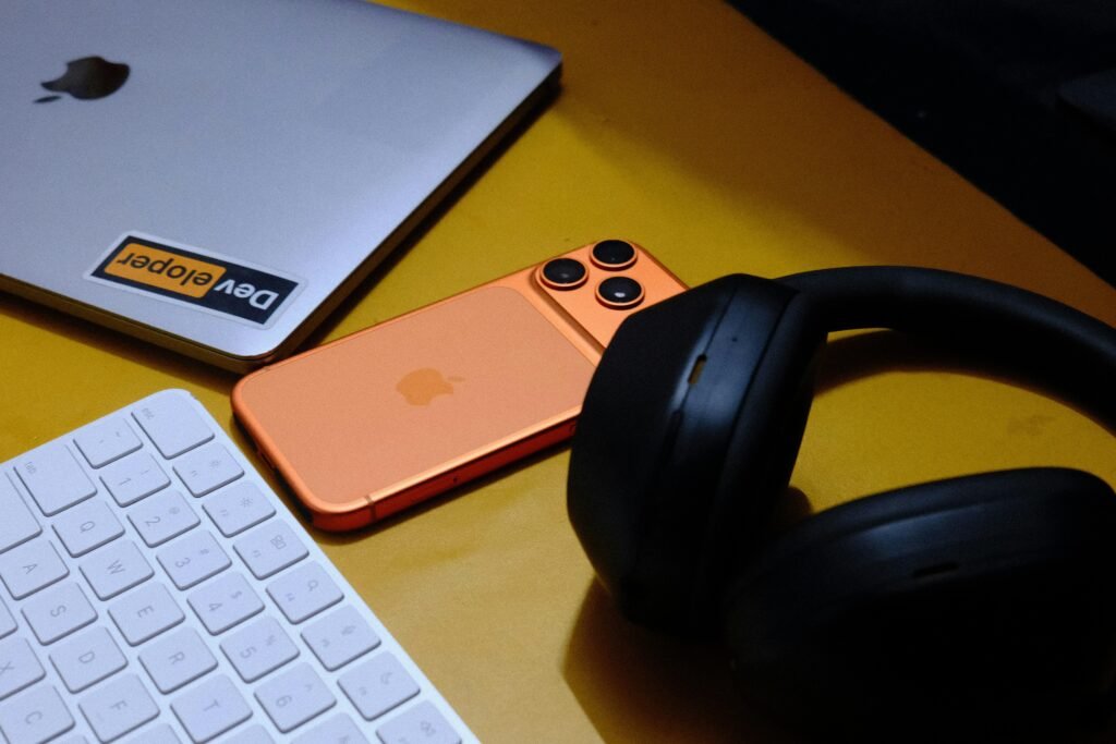 Laptop, Smartphone, Tastatur und Kopfhörer nebeneinander auf einer gelben Fläche arrangiert, Fokus auf technischen Geräten