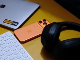 Laptop, Smartphone, Tastatur und Kopfhörer nebeneinander auf einer gelben Fläche arrangiert, Fokus auf technischen Geräten