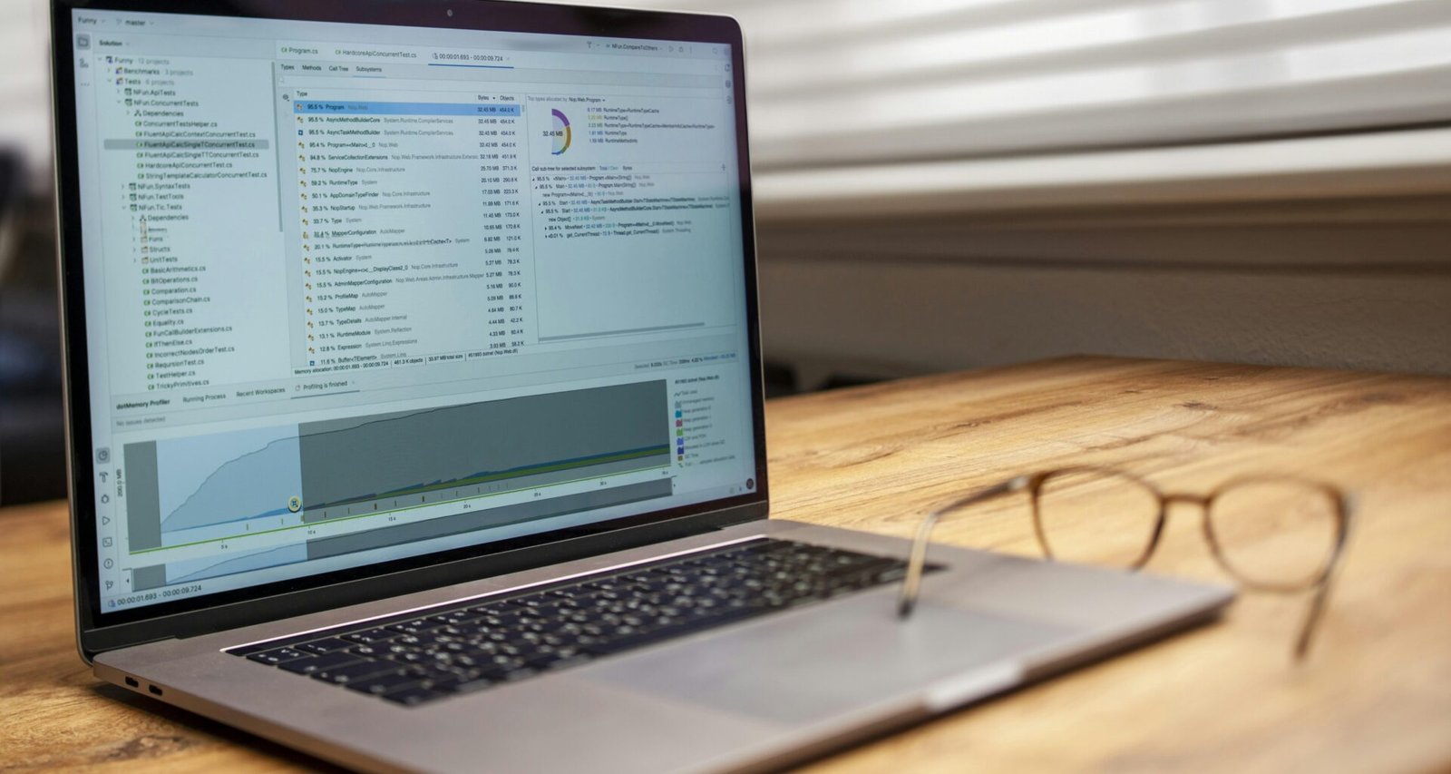 Offener Laptop und eine Brille liegen auf einem Holztisch, typischer Arbeitsplatz für digitale Projekte im Büroalltag.